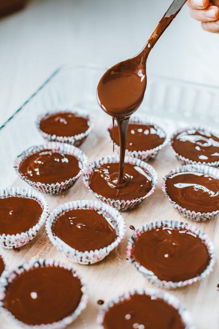 A person pouring rich chocolate into muffin cups, preparing delicious desserts.